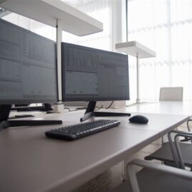A modern dual monitor desktop workstation in a bright NZ office, the desk-bound side of the desktop versus laptop choice
